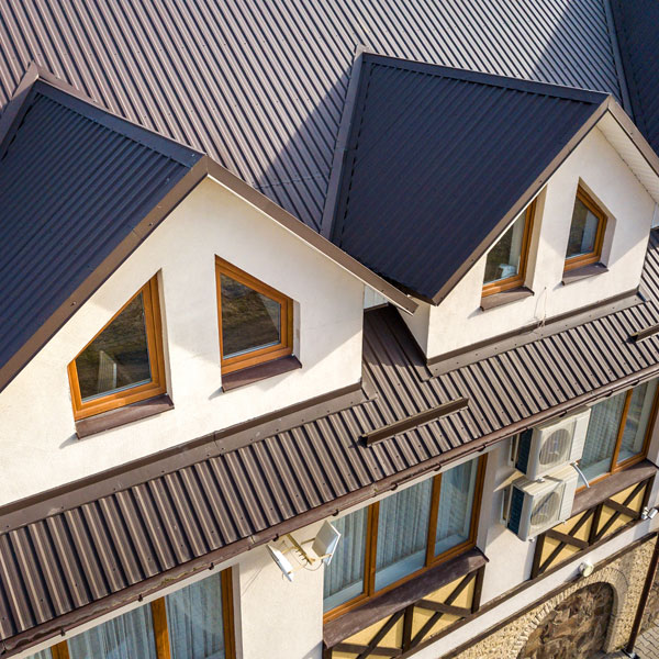 Close Up Aerial View Of Building Attic Rooms Exterior On Metal Shingle Roof, Stucco Walls And Plastic Windows.
